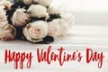 Happy Valentine`s Day text sign and white roses bouquet in light on wooden background. Valentines day floral greeting card Royalty Free Stock Photo