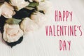 Happy Valentine`s Day text sign and white roses bouquet in light on wooden background. Valentines day floral greeting card Royalty Free Stock Photo