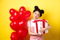 Happy Valentines day. Cute asian girl hugging surprise gift from boyfriend, standing near lovely red heart balloons and Royalty Free Stock Photo