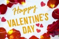 Happy Valentines Day gold text greeting card with red rose petals and shiny hearts bokeh on white wooden Background Royalty Free Stock Photo