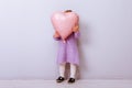 Happy valentines day heart. Baby girl covered her face by a pink heart balloon on a light purple background Royalty Free Stock Photo