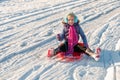 Happy, vibrantly dressed young girl with blue ear muffs sledging down a slope