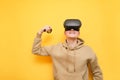 Happy VR gamer winner stands on yellow background, smiles and shows biceps. Portrait of a guy in a VR helmet smiling isolated on