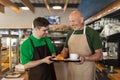 Happy waiter with Down syndrome serving coffee with help of his collegue at cafe.