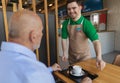 Happy waiter with Down syndrome serving coffee to senior customer at cafe. Royalty Free Stock Photo