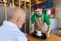 Happy waiter with Down syndrome serving coffee to senior customer at cafe. Royalty Free Stock Photo