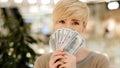 Happy wealthy successful middle aged adult caucasian business woman looking at camera holding fan of money hiding behind Royalty Free Stock Photo