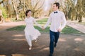 Happy wedding couple charming groom and blonde bride running with joined hands on city park road Royalty Free Stock Photo