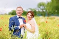 Happy wedding couple in pink poppy field. Beautiful bride in white dress and groom kissing and having fun in flower Royalty Free Stock Photo