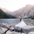 Happy wedding couple is standing in front of lake surrounded with mountains on the huge rock Royalty Free Stock Photo