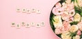 Happy wedding lettering on the wooden squares with letters on the pink background and big round box with red flowers and