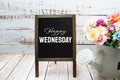 Happy Wednesday text on blackboard easel with flower bouquet on wooden background