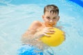 Happy white caucasian boy swimming in clear blue water pool and plays with yellow ball Royalty Free Stock Photo