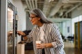 Happy white-haired woman using vending machine while drinking coffee Royalty Free Stock Photo