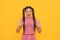 Happy winking girl child show double ring gesture yellow background, OK