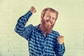 Happy winner. Portrait of a bearded guy celebrating fists up casual blue shirt man winner dance gesture isolated white brick wall