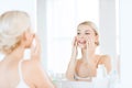 Happy woman applying cream to face at bathroom Royalty Free Stock Photo