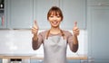 happy woman in apron showing thumbs up in kitchen