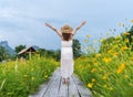 Woman with arm raised on wooden bridge with yellow cosmos flower field