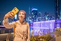 Woman blogger takes a beautiful selfie photo against the background of an artificial waterfall illuminated in neon light