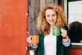 Happy woman with blonde curly fluffy hair charming blue eyes holding two mugs of coffee going to treat her friends with coffee hav Royalty Free Stock Photo