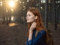 Happy woman in a blue shirt travels in a pine forest and the sunset in the distance