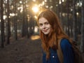 Happy woman in a blue shirt travels in a pine forest and the sunset in the distance