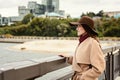 Happy woman in a brown hat and beige coat stands at the edge of the embankment and gazing into the distance. the concept of waitin