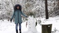 Happy woman building snowman at winter forest. Smiling woman looking into camera after finish built snow man at snowy Royalty Free Stock Photo