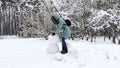 Happy woman building snowman at winter forest. Young girl having active leisure at snowy park. Cheerful female having