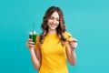 Happy woman choose unhealthy cake holding smoothie detox juice on blue background