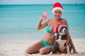 Young happy woman in christmas hat sitting at the beach with her friend amstaff dog Royalty Free Stock Photo