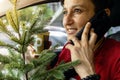 Happy woman with Christmas tree is talking on phone in car while drinking coffee Royalty Free Stock Photo