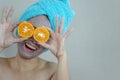 Happy woman with a clay mask with biting slice of orange.