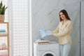 Happy woman with clothes near washing machine in bathroom. Laundry day Royalty Free Stock Photo