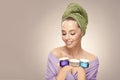 Happy woman with clean fresh skin hold a different of face care creams, wearing in bathrobe and towel on head Royalty Free Stock Photo