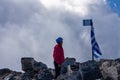 Happy woman with climbing equipment on cloud covered mountain summit of Mytikas Mount Olympus, Greece. Greek flag on top Royalty Free Stock Photo