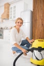 Happy woman crouched near vacuum cleaner