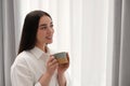 Happy woman with cup of drink near window at home, space for text. Lazy morning Royalty Free Stock Photo