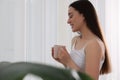 Happy woman with cup of drink near window indoors, space for text. Lazy morning Royalty Free Stock Photo