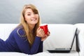 Happy woman with cup of tea or coffee using laptop lying on sofa, modern technology Royalty Free Stock Photo