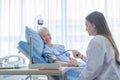 Happy woman doctor checking blood pressure test of sick old female senior elderly patient lying in bed in hospital ward room in Royalty Free Stock Photo