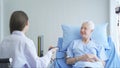 Happy woman doctor checking blood pressure test of sick old female senior elderly patient lying in bed in hospital ward room in Royalty Free Stock Photo