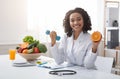 Happy woman doctor holding orange and barbell in clinic Royalty Free Stock Photo