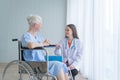 Happy woman doctor talking to disabled old female senior elderly patient on wheelchair in hospital ward room in medical and Royalty Free Stock Photo