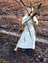 Happy woman in a dress dances barefoot on a muddy field, holding reeds in her hands