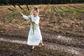 Happy woman in a dress dances barefoot on a muddy field, holding reeds in her hands