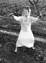 Happy woman in a dress dances barefoot on a muddy field, holding reeds in her hands