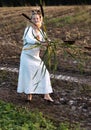 Happy woman in a dress dances barefoot on a muddy field, holding reeds in her hands