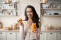 Happy woman drinking orange juice and holding fruit, standing in kitchen interior, free space Royalty Free Stock Photo